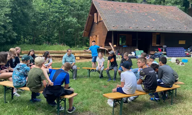 Kinder mit Lehrer sitzen im Freien auf Bierbänken im Kreis